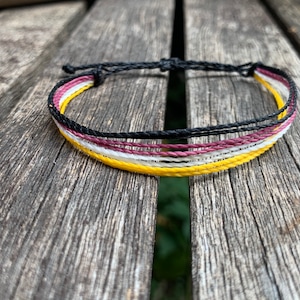 May include: A multi-colored friendship bracelet with black, white, yellow, and burgundy threads.