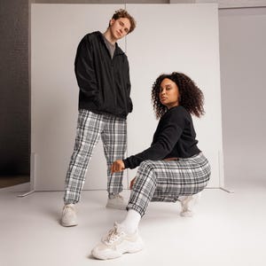 Könnte beinhalten: Zwei Personen tragen schwarze Jacken und schwarze Sweatshirts mit passenden schwarz-weiß karierten Hosen. Beide tragen weiße Turnschuhe. Der Hintergrund ist eine schlichte weiße Wand.