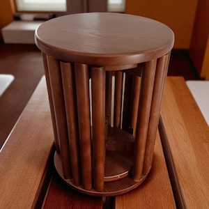 May include: A brown wooden side table with a cylindrical design. The table features a round top and base, connected by vertical wooden rods. The table is approximately 18 inches tall and 14 inches in diameter.