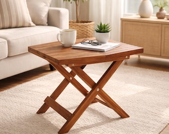 May include: A small, square, folding wooden side table with a warm brown finish. The table has an X-shaped base and a slatted top. A white mug, glasses, a small plant, and a book rest on the table. The table is 24 inches long.