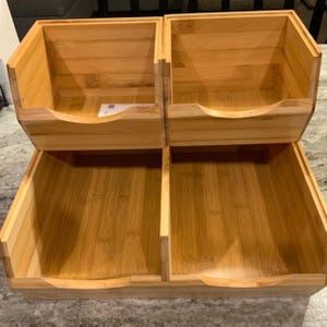 May include: A bamboo organizer with four compartments. The top two compartments are stacked above the bottom two. Each compartment has a curved cutout for easy access. The natural wood grain is visible throughout the organizer.