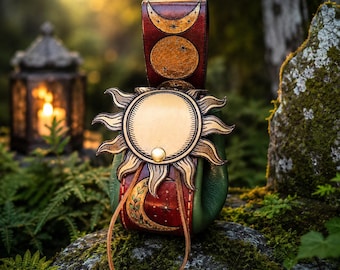 Pode incluir: Uma bolsa de couro verde e castanho-avermelhado com fecho de aba em forma de sol e um botão de pressão de latão. O exterior é decorado com motivos celestiais em relevo, incluindo uma lua crescente, estrelas e um padrão de videira.