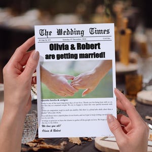 Puede incluir: Un anuncio de boda estilo periódico, titulado "The Wedding Times", sostenido por manos. El titular dice "¡Olivia & Robert se casan!" con una foto de manos entrelazadas. El texto incluye una fecha y buenos deseos.