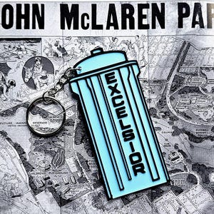 May include: A light blue keychain in the shape of a trash can with the word "EXCELSIOR" in black. The keychain is attached to a silver chain and ring. The background is a black and white map.