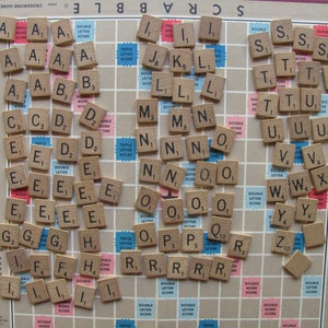 Pode incluir: Um close-up de um jogo de Scrabble em andamento. O tabuleiro está cheio de peças de letras, incluindo S, A, T, E, O e N. As peças são organizadas em uma variedade de cores, incluindo marrom, branco e preto. O tabuleiro é feito de madeira e tem um acabamento marrom claro.