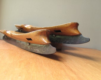 May include: A pair of vintage wooden ice skates with metal blades. The skates are brown and have a worn, rustic look. The blades are rusty and have a patina.