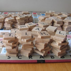 May include: A close-up of a Scrabble game in progress. The tiles are stacked in columns, spelling out the words "TRAIL", "A", "H", and "L". The board is green and has a red border. The game is played on a wooden table.