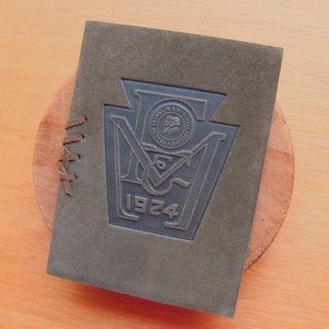 May include: A dark green leather-bound book with a blue embossed seal featuring the letters "MCM" and the year "1924".