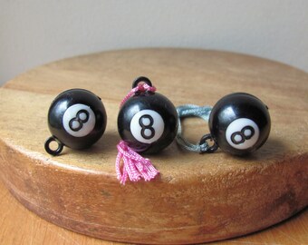 May include: Three black and white 8-ball charms with pink tassels. The charms are made of plastic and have a shiny finish.