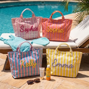 May include: Four striped tote bags with personalized names in raised lettering, including Sophie, Kelly, and Emma. The bags are accompanied by a blue polka-dot swimsuit, a light blue swim cap, a tube of sunscreen, and brown sunglasses.