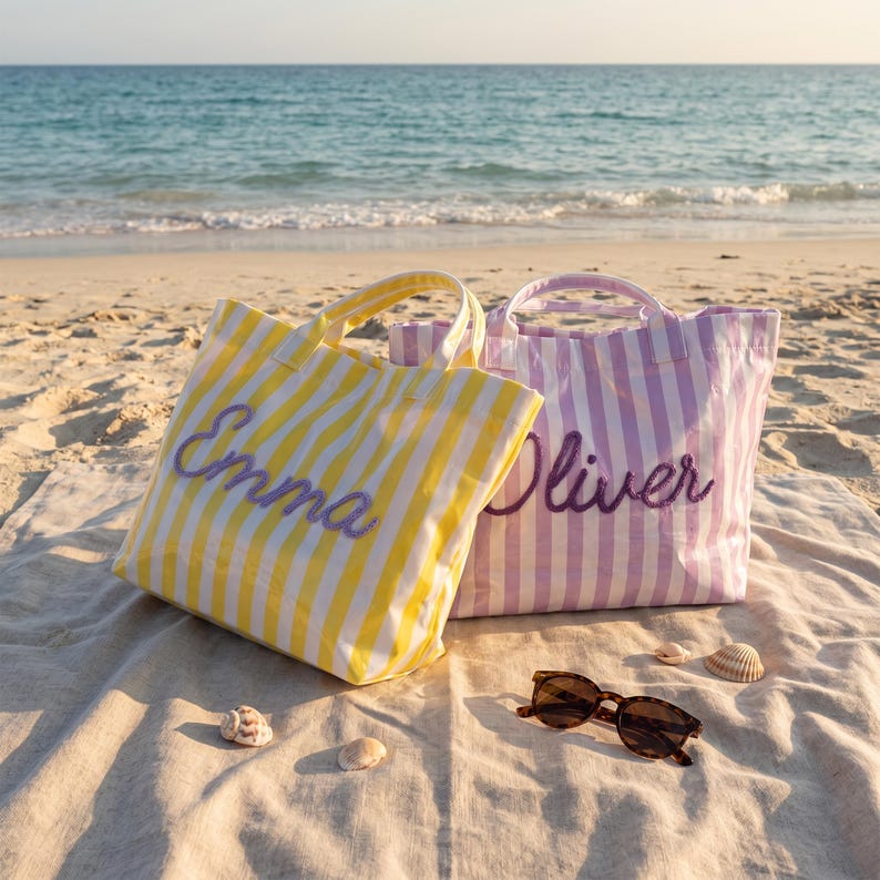 May include: Two striped tote bags with handles, one yellow and white with the name Emma embroidered in purple, and one lavender and white with the name Oliver embroidered in purple, accompanied by a pair of brown tortoiseshell sunglasses.