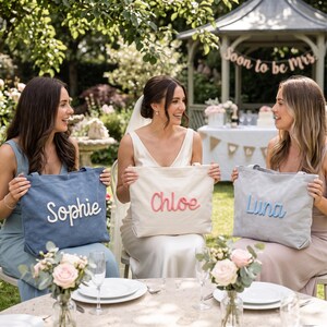 May include: Three rectangular canvas tote bags with custom names in raised lettering. The left bag is blue with white text reading Sophie, the center bag is white with pink text reading Chloe, and the right bag is light gray with blue text reading Luna.