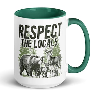 Peut inclure: Mug en céramique blanche avec intérieur et anse verts. Le mug présente un dessin d'ours, de cerf, de renard et de lapin avec le texte "RESPECT THE LOCALS" en noir. Le design comprend des arbres verts.