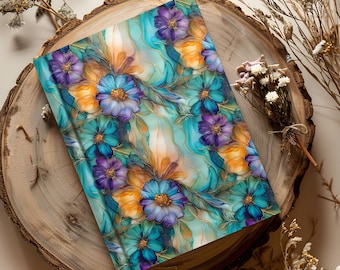 May include: A floral journal with a vibrant design featuring blue, purple, and orange flowers on a teal background. The journal is set on a wooden slice, with dried flowers and foliage in the background.