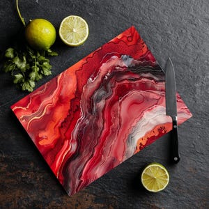 May include: A rectangular cutting board with a red and white agate design. A black knife, two lime halves, and cilantro sprigs are arranged on a dark surface. The board features a marbled pattern with gold accents.