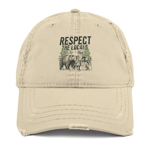 May include: A distressed beige baseball cap with the text "RESPECT THE LOCALS" above a graphic of a bear, deer, and trees. The cap has a pre-worn look with distressed edges.
