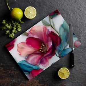 Puede incluir: Tabla de cortar rectangular con un diseño floral en tonos rosa, rojo y turquesa. Un cuchillo de acero inoxidable con mango negro descansa sobre la tabla. Limas y cilantro están dispuestos alrededor.