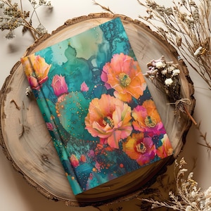 May include: A hardcover journal featuring a vibrant floral design with orange, pink, and yellow flowers, and a teal background. The journal is placed on a wooden slice with dried flowers.