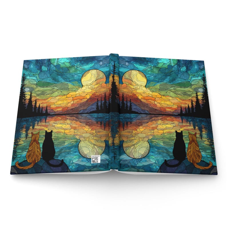 May include: A hardcover journal featuring a stained-glass style landscape with a sunset, silhouetted pine trees, and a reflective lake. Two cats, one orange and one black, sit on each side of the cover, looking toward the horizon.
