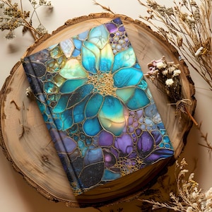 May include: A hardback journal with a floral design in shades of blue, teal, purple, and gold. The cover features a large flower with intricate details and a textured appearance. The journal is resting on a wooden slice.
