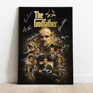 May include: A framed poster featuring the movie "The Godfather." The poster has a black background with the film's title in gold. The image includes several actors and signatures. The poster is displayed on a white wall.