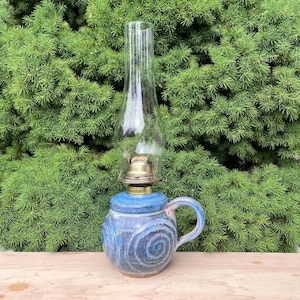 May include: A white ceramic mug with a black handle and the text "But First, Coffee" in a bold, black font. The mug is set against a blurred background, suggesting a cozy setting.