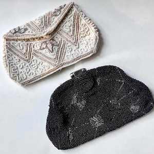 May include: Two vintage beaded evening bags. One is off-white with a geometric pattern and floral accents. The other is black with a silver clasp and a geometric design. Both bags are on a white background.