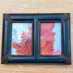 May include: A rectangular double picture frame with a dark green finish and a rope-textured inner border. The frame features decorative corner accents and contains two separate glass panels displaying a vibrant red and orange floral print.