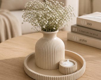 May include: A beige ribbed ceramic vase filled with white baby's breath flowers, accompanied by a matching small ribbed candle holder containing a white tea light, all arranged on a circular beige ribbed tray with a consistent vertical texture.