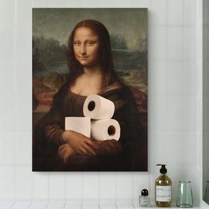 May include: A framed canvas print of the Mona Lisa holding three rolls of toilet paper. The artwork is displayed in a modern bathroom setting with white tile and a white sink.