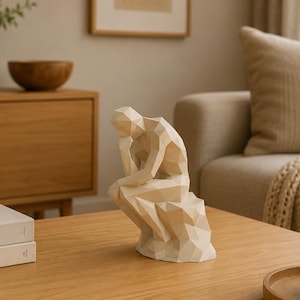 May include: A cream-colored, low-poly geometric sculpture of a seated figure in a contemplative pose, resting one hand on its chin. The figure is composed of angular, faceted planes, creating a sharp, modern appearance with a smooth, matte finish.