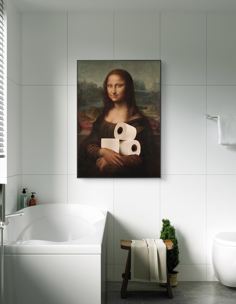 May include: A framed print of the Mona Lisa holding three rolls of toilet paper. The artwork is displayed in a modern bathroom setting with white tile walls and a white bathtub.