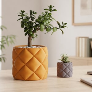 May include: A large mustard yellow cylindrical planter with a quilted diamond pattern containing a green jade plant, and a smaller matching dark gray planter with a quilted diamond pattern containing a small succulent plant.