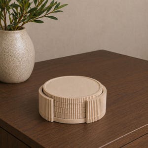 May include: A stack of four circular beige coasters with a ribbed, vertical texture on the edges, housed within a matching cylindrical holder that features the same fluted design, creating a uniform and cohesive set for surface protection.