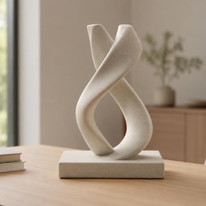 May include: A light beige, speckled stone sculpture featuring a continuous, twisting loop design that rises from a solid, rectangular base. The surface has a matte, textured finish, and the form creates an open, fluid shape that curves upward.