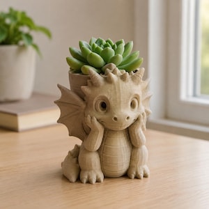Può includere: Un vaso per piante color beige chiaro dalla texture definita a forma di drago, contenente una piccola pianta succulenta verde nella parte superiore. Il drago ha grandi occhi, piccole ali e le mani appoggiate sulle guance da seduto.