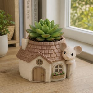 May include: A decorative planter shaped like a small house with a brown shingled roof and a cream-colored exterior. A sculpted white mouse figure clings to the side of the house. A green succulent plant is potted in the top of the structure.