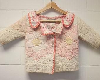 May include: A white quilted jacket with a pink floral pattern and a pink scalloped collar. The jacket has a button closure and a pink trim.