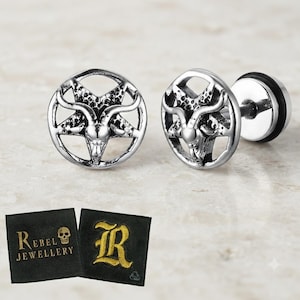 Op de afbeelding: Een paar zilverkleurige oorknopjes met een cirkelvormig pentagramontwerp en een geitenkopmotief in het midden. De oorbellen worden vergezeld door een zwart vierkant label met de tekst Rebel Jewellery en een afbeelding van een schedel.