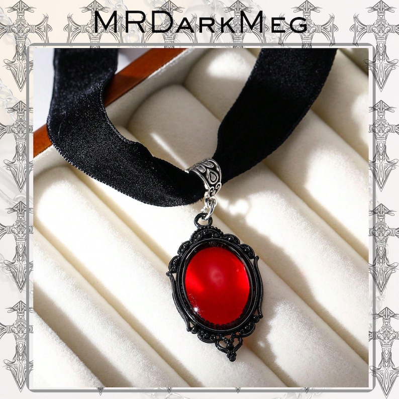 May include: Black velvet choker necklace with a red oval pendant. The pendant has a black filigree frame and a bright red center. The necklace is displayed in a white jewelry box. The text "MRDARKMEG" is at the top.