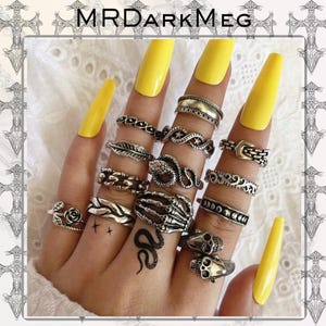 May include: A collection of silver rings with various designs, including a snake, a skeleton hand, and a rose. The rings are displayed on a hand with yellow nail polish. The brand name "MRDARKMEG" is at the top.