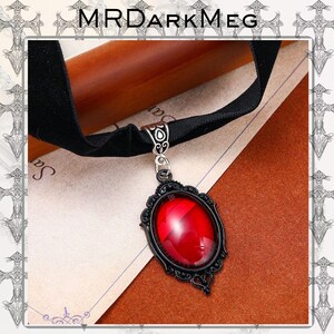 May include: Black velvet choker necklace with a decorative pendant. The pendant features a large, oval, red gemstone set in a black filigree frame. The brand name "MRDARKMEG" is at the top of the image.