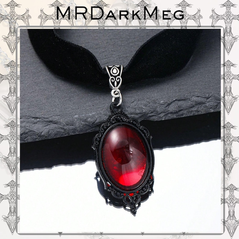 May include: Black velvet choker necklace with a gothic-style pendant. The pendant features a large, oval, deep red gemstone set in a black filigree frame. The necklace is a dark, elegant accessory.