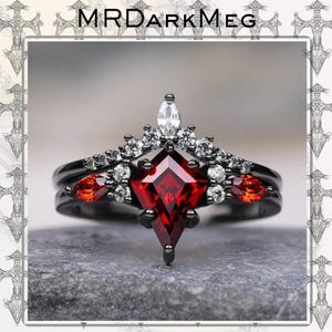 Könnte beinhalten: Schwarzer Ring mit einem großen, roten, rautenförmigen Mittelstein. Der Ring ist mit kleineren weißen und orangefarbenen Edelsteinen verziert. Einzigartiges, gotisches Design. Der Text "MRDARKMEG" ist oben im Bild zu sehen.
