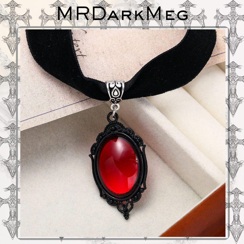 May include: Black velvet choker necklace with a decorative pendant. The pendant features a large, oval, red gemstone set in a black filigree frame. The necklace has a silver-toned clasp and a decorative silver-toned bail. The brand name "MRDARKMEG" is at the top.