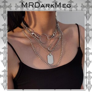 May include: A multi-layered silver necklace with a dog tag pendant, a large ring, and a safety pin design. The necklace is worn over a black tank top. The brand name "MRDARKMEG" is at the top of the image.
