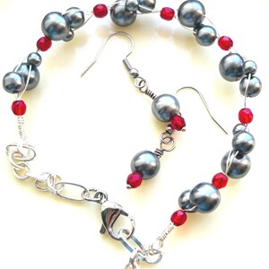May include: A jewellery set comprising a bracelet and matching earrings. The bracelet and earrings are made with grey, spherical beads and small red beads, strung together with silver wire. The bracelet has a silver clasp.