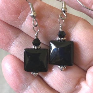 May include: A pair of drop earrings featuring smooth, square black beads suspended from silver-toned metal hooks. Each earring includes a small, faceted black bead above the square piece, accented by tiny silver-toned metal beads at the top and bottom.