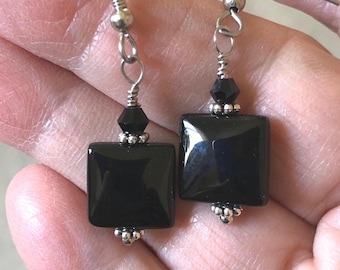 May include: A pair of drop earrings featuring smooth, square black beads suspended from silver-toned metal hooks. Each earring includes a small, faceted black bead above the square piece, accented by tiny silver-toned metal beads at the top and bottom.