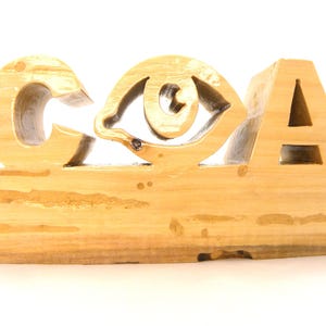 May include: A wooden sign with the letters "COA" carved into it. The "O" is shaped like an eye.